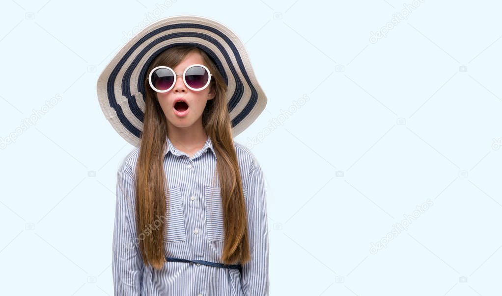 Young blonde toddler wearing hat and sunglasses scared in shock with a surprise face, afraid and excited with fear expression