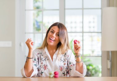 Duygu tezahürat genç kadın ev gurur çığlık macarons yeme ve zafer ve başarı çok heyecanlı, kutluyor