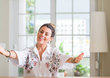 Genç kadın evde sarılmak için kollarını açarak gülümseyen kamera bakıyor. Neşeli ifade kucaklayan mutluluk.