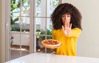 Afrikalı-Amerikalı kadın evde ile lezzetli biberli pizza yemeye hazır açık el dur işareti ile ciddi ve kendine güvenen ifade, savunma hareketi yapıyor