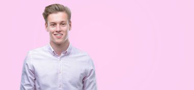 Genç yakışıklı sarışın adam ayakta ve diş gösterilen kendine güvenen bir gülümsemeyle gülümseyerek mutlu bir yüz ile