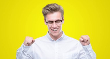 Genç yakışıklı sarışın adam silah ile başarı için heyecanlı zafer kutluyor gülümseyen kaldırdı. Kazanan kavramı.