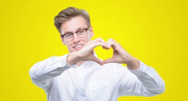 Kalp simgesi ve elleriyle şekil gösterilen aşık gülümseyen genç yakışıklı sarışın adam. Romantik kavramı.