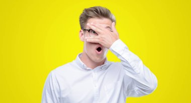 Mahcup ifadeyle parmaklarımın arasından seyir yüz ve gözler el ile kapsayan şok bakmak genç sarışın yakışıklı.