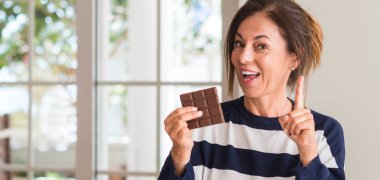 Orta yaşlı kadın çikolatayı bir fikir ya da soru işaret parmağı gülen yüz, bir numara ile sürpriz yemek