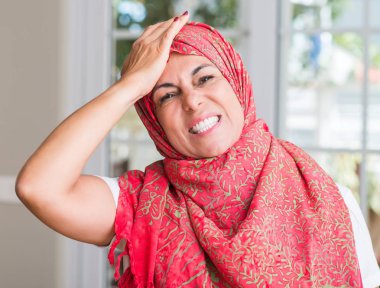 Orta yaşlı Müslüman kadının kafasına, utanç ve sürpriz yüz ile şok el ile vurguladı hijab giyen öfkeli ve sinirli. Korku ve hata için üzgün.