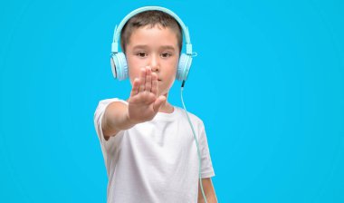 Koyu saçlı küçük çocuk müzik dinleme ile kulaklıklar ile açık el dur işareti ile ciddi ve kendine güvenen ifade, savunma hareketi yapıyor