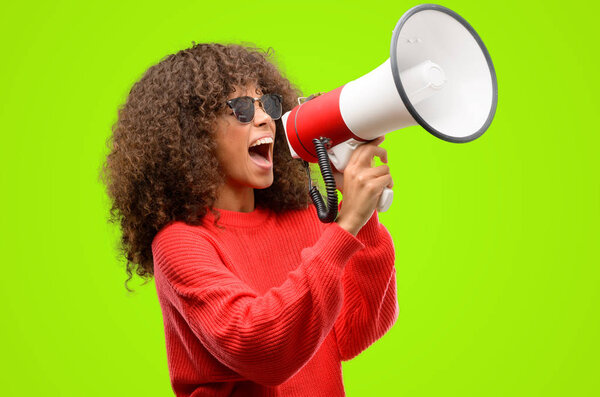 African american woman wearing sunglasses communicates shouting loud holding a megaphone, expressing success and positive concept, idea for marketing or sales