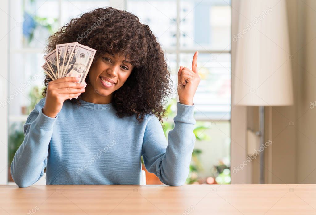 African american woman holding dollar bank notes very happy pointing with hand and finger to the side
