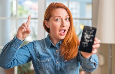 Kırık smartphone sürpriz bir fikir ya da soru işaret parmağı ile gülen yüz, bir numara tutan Kızıl saçlı kadın