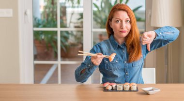 Yemek çubukları kullanarak kızgın yüzü, eksi işareti aşağı antipati başparmak ile gösterilen, ret kavramı ile suşi yemek Kızıl saçlı kadın