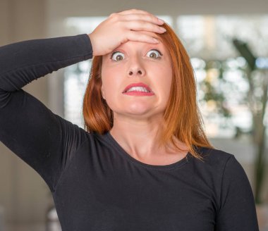 Kızıl saçlı kadın evde kafasına, utanç ve sürpriz yüz, öfkeli ve sinirli ile şok el ile vurguladı. Korku ve hata için üzgün.