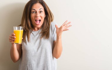 Orta yaş kadın büyük gülümseme ile çığlık zaferini kutluyor ve ellerini kaldırdı bir cam çok mutlu ve heyecanlı, kazanan ifadesinde portakal suyu içme
