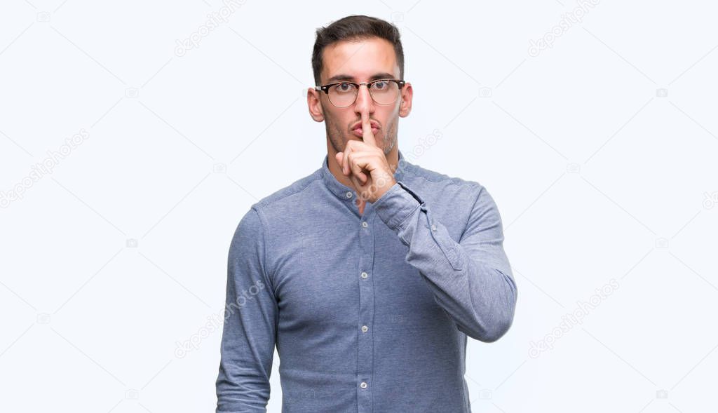 Handsome young elegant man wearing glasses asking to be quiet with finger on lips. Silence and secret concept.