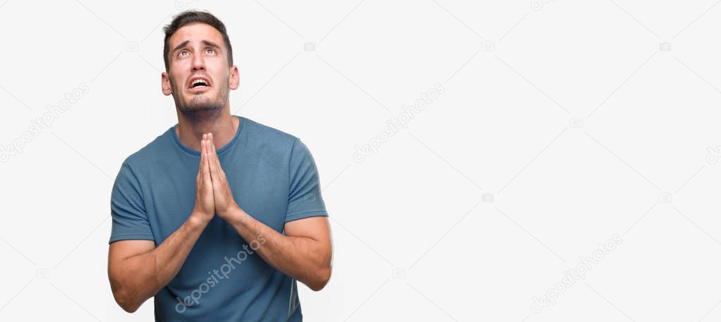 Handsome young casual man begging and praying with hands together with hope expression on face very emotional and worried. Asking for forgiveness. Religion concept.