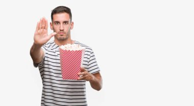 Yakışıklı genç adam yeme patlamış mısır açık eliyle dur işareti ile ciddi ve kendine güvenen ifade, savunma hareketi yapıyor