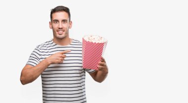 Yakışıklı genç adam yeme patlamış mısır el ve parmak ile işaret çok mutlu