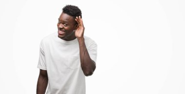 Beyaz t-shirt el ile gülümseyen bir işitme söylenti ya da dedikodu için dinleme kulak üzerinde giyen genç Afro-Amerikan adam. Sağırlık kavramı.