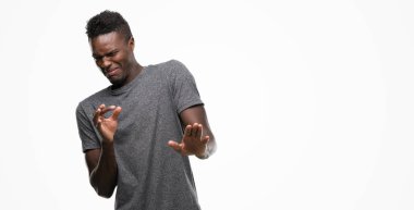 Young african american man wearing grey t-shirt disgusted expression, displeased and fearful doing disgust face because aversion reaction. With hands raised. Annoying concept. clipart