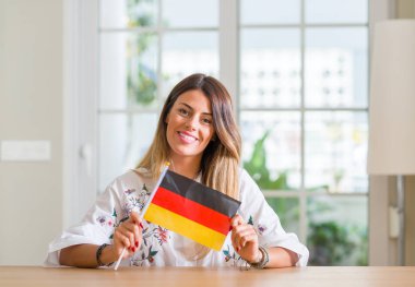 Genç kadın evde duran ve diş gösterilen kendine güvenen bir gülümsemeyle gülümseyerek mutlu bir yüz ile Almanya bayrağı tutarak