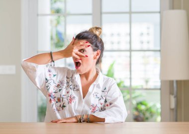 Genç kadın evde yüz ve gözler el ile kapsayan şok mahcup ifadeyle parmaklarımın arasından seyir bakmak.