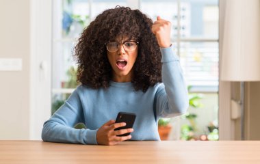 Akıllı telefon kullanan güzel Afrikalı-Amerikalı kadın rahatsız ve boşa çıkarmak ile öfke, çılgın da yükseltilmiş el ile bağırmaya kavramı öfke
