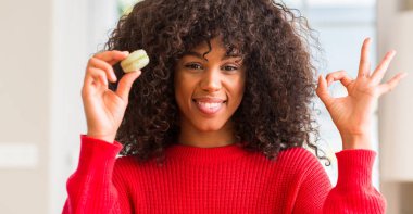 Parmak, mükemmel sembolü ile ok işareti yapıyor macaron tutan Afrikalı-Amerikalı kadın