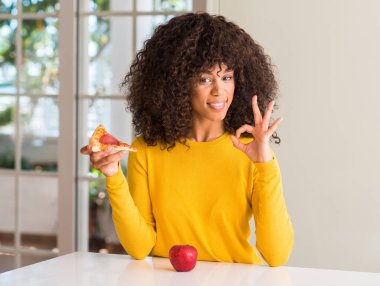 Afrikalı-Amerikalı kadın parmakları, mükemmel sembolü olan ok işareti yapıyor elma ve pizza dilimi arasında seçme