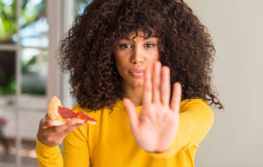 Afrikalı-Amerikalı kadın ile dilim biberli pizza yemeye hazır açık el dur işareti ile ciddi ve kendine güvenen ifade, savunma hareketi yapıyor