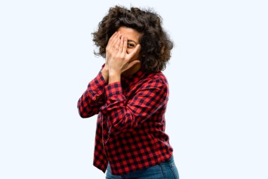 Confusedly geniş seyir elleriyle yüzünü kapsayan parmaklarının arasından, utangaç göz atmayı sahip gülümseyen güzel Arap kadın