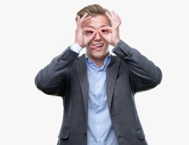 Genç yakışıklı sarışın iş adamı, dilini parmaklarının arasından baktığını yapışmasını dürbün gibi ok jest yapıyor. Deli ifade.