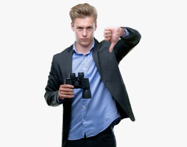 Genç yakışıklı sarışın adam kızgın yüzü, eksi işareti aşağı antipati başparmak ile gösterilen, ret kavramı dürbünle bakarak