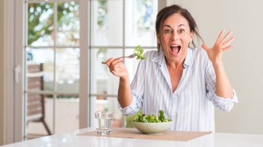 Taze salata bir kase içinde evde çok mutlu ve heyecanlı, kocaman bir gülümseme ile çığlık ve ellerini kaldırdı kazanan ifade kutluyor zafer yemek kadın orta yaşlı