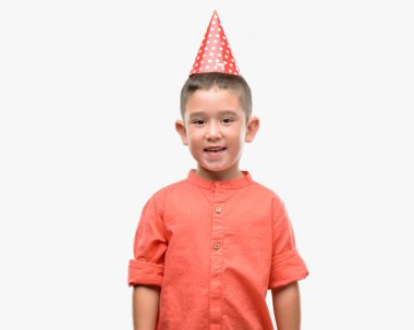 Koyu saçlı küçük çocuk ayakta ve diş gösterilen kendine güvenen bir gülümsemeyle gülümseyerek mutlu bir yüz ile Doğum günü şapkası