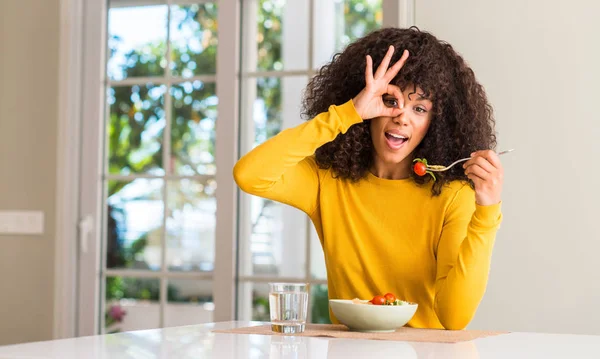 非洲裔美国妇女吃面食沙拉与愉快的面孔微笑做 标志用手在眼睛看通过手指 — 图库照片