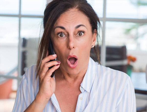 Middle aged woman using smartphone scared in shock with a surprise face, afraid and excited with fear expression