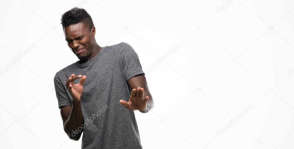 Young african american man wearing grey t-shirt disgusted expression, displeased and fearful doing disgust face because aversion reaction. With hands raised. Annoying concept.