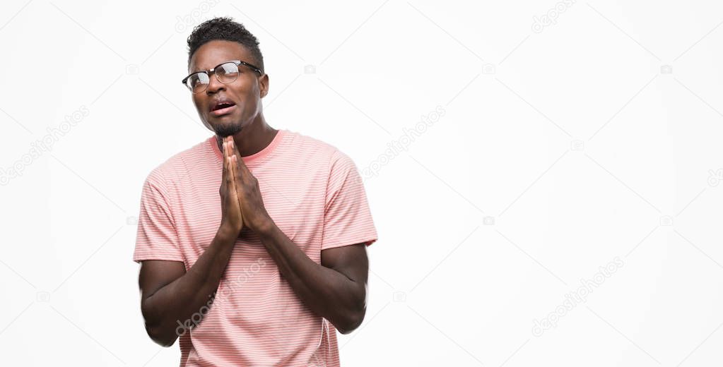 Young african american man wearing pink t-shirt begging and praying with hands together with hope expression on face very emotional and worried. Asking for forgiveness. Religion concept.