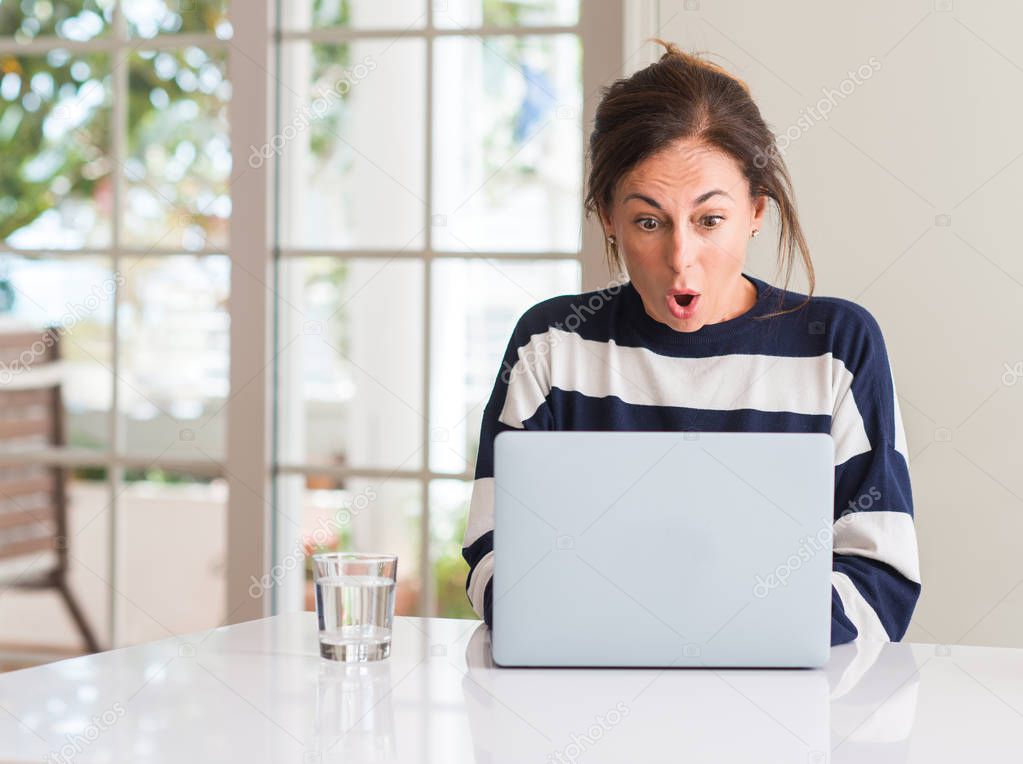 Middle aged woman using laptop at home scared in shock with a surprise face, afraid and excited with fear expression