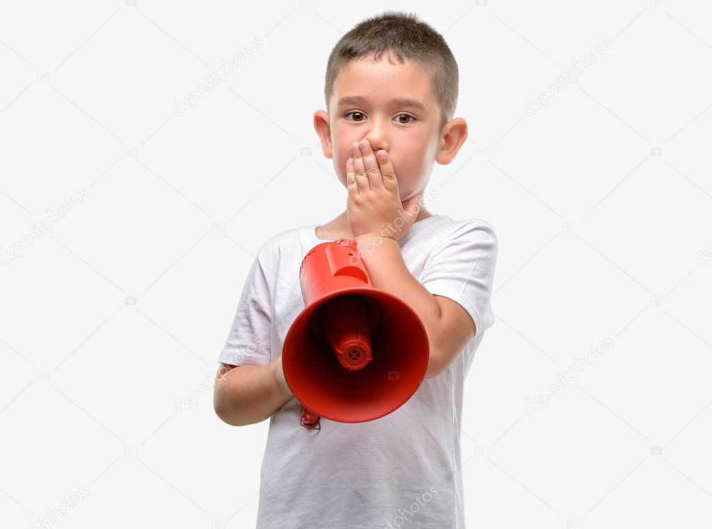 Dark haired little child holding megaphone cover mouth with hand shocked with shame for mistake, expression of fear, scared in silence, secret concept