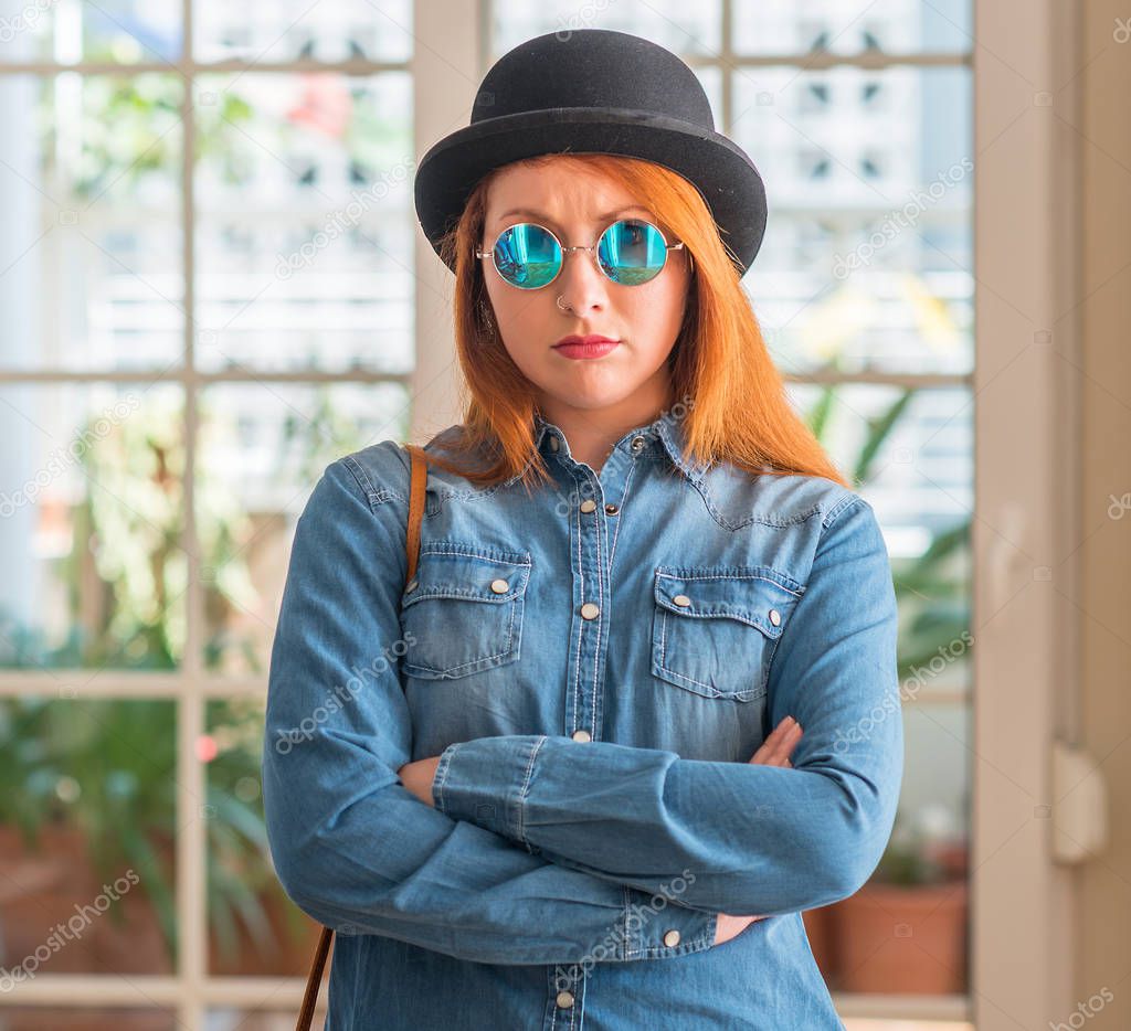 Stylish redhead woman wearing bowler hat and sunglasses skeptic and nervous, disapproving expression on face with crossed arms. Negative person.
