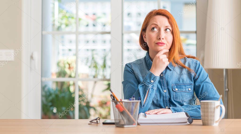 Redhead woman studying at home serious face thinking about question, very confused idea