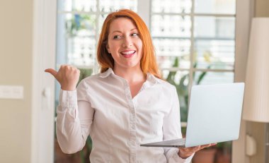 Kızıl saçlı kadın evde bilgisayar dizüstü kullanarak el ve parmak ile mutlu yüz gülümseyen ile yukarı dönük