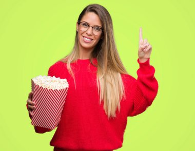 Güzel genç kadın bir fikir ya da soru işaret parmağı gülen yüz, bir numara ile sürpriz patlamış mısır yemek