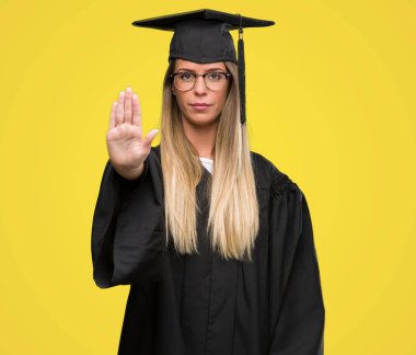 Dur işareti ile ciddi ve kendine güvenen ifade, savunma hareketi yaparken açık el ile gözlük ve mezuniyet elbise giyen güzel genç kadın