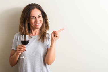 Orta yaş kadın el ve parmak ile tarafına işaret çok mutlu bir bardak kırmızı şarap içme