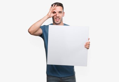 Reklam afişi ile ok işareti ile el parmaklarının arasından seyir göze yapıyor gülümseyen mutlu yüz tutan yakışıklı genç