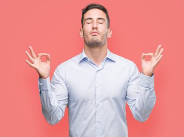 Yakışıklı genç işadamı rahatla ve gülümseyen gözlerle kapalı parmak jestle meditasyon yapıyor. Yoga kavramı.