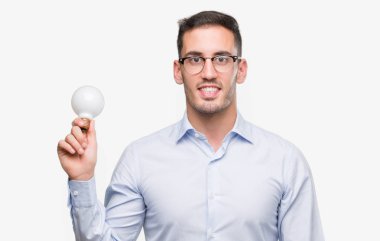 Ampul fikir olarak duran ve diş gösterilen kendine güvenen bir gülümsemeyle gülümseyerek mutlu bir yüz ile tutarak yakışıklı genç