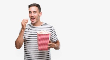 Bir gülen surat konumu olan patlamış mısır yemek ve diş gösterilen kendine güvenen bir gülümseme ile gülümseyen yakışıklı delikanlı